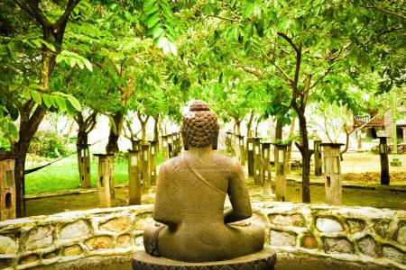 Foto de Una estatua de Buda meditando frente al jardín verde y el templo - Imagen libre de derechos