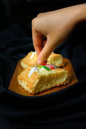 Téléchargez les photos : Le doigt humain mange des morceaux moelleux de gâteau sur un plateau en bois sur fond de satin noir - en image libre de droit