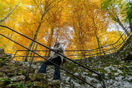Foto de Una toma de ángulo bajo de una hembra subiendo escaleras de piedra en el parque nacional de los lagos de Plitvice en otoño - Imagen libre de derechos