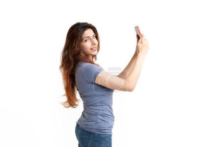 Téléchargez les photos : Un plan studio d'une femme souriante prenant un selfie et regardant la caméra sur un fond blanc - en image libre de droit