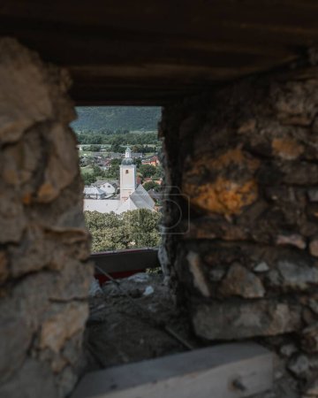 Téléchargez les photos : Une vue du village Beckov depuis une petite fenêtre en pierre arbres et bâtiments autour - en image libre de droit