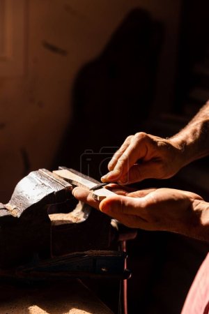 Téléchargez les photos : Un gros plan des mains de l'homme lissant un morceau de bois avec un outil sous la lumière du soleil - concept d'artisanat - en image libre de droit