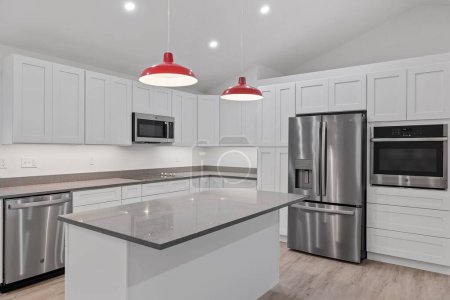 Foto de El interior de una cocina con armarios blancos, lámparas colgantes rojas, un suelo de parquet y electrodomésticos - Imagen libre de derechos