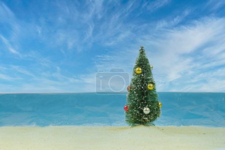 Foto de Un árbol de Navidad en miniatura con bolas frente a un fondo de playa falso - Imagen libre de derechos