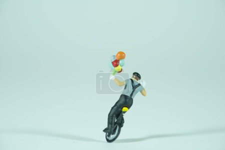 Foto de Un payaso cabalga sobre un monociclo, sostiene en una mano varios globos de colores, aislados sobre fondo claro - Imagen libre de derechos