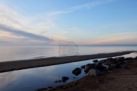 Foto de Las aguas azules de un mar tranquilo y las piedras en la orilla bajo un cielo azul - Imagen libre de derechos