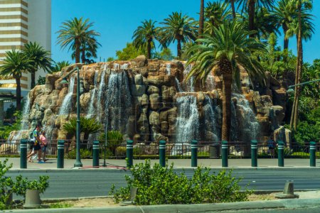 Téléchargez les photos : Le volcan artificiel du Mirage Hotel and Casino de Las Vegas, entouré de palmiers verts et de touristes passant par là - en image libre de droit