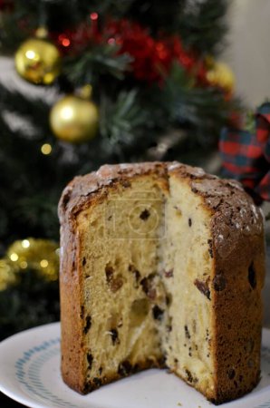 Foto de Una toma vertical de un pastel de Navidad (Panettone) con pasas en el fondo del árbol de Navidad - Imagen libre de derechos