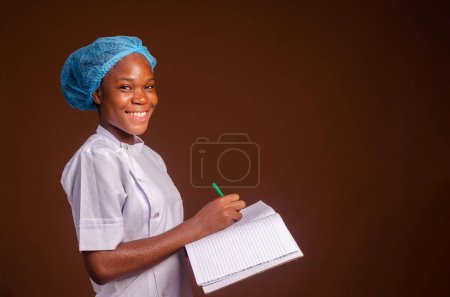 Photo for A closeup of a beautiful nurse smiling and taking notes on a brown background - Royalty Free Image