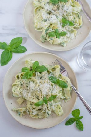 Photo for A vertical shot of two plates of pesto pasta with basil and parmesan cheese on the table - Royalty Free Image