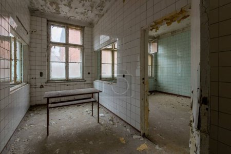 Photo for An empty decaying room with a table and torn ceramic walls in an abandoned place - Royalty Free Image