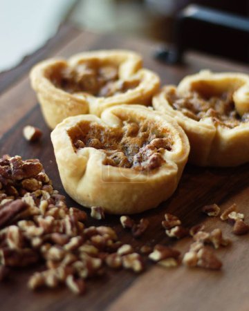 Photo for A vertical shot of pecan butter tart on the wooden surface next to a bunch of pecans - Royalty Free Image