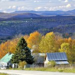 Quiet country road in Northeast Kingdom of rural Vermont with sweeping view of mountains, farm buildings, and colorful autumn foliage.