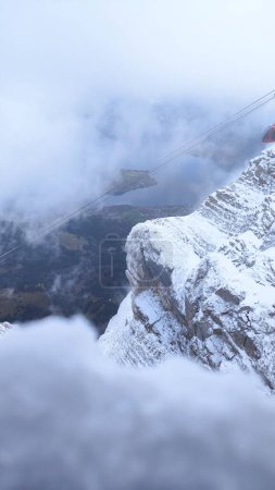 Téléchargez les photos : Un beau plan vertical de brouillard dense recouvrant les montagnes couvertes de neige rocheuse - en image libre de droit