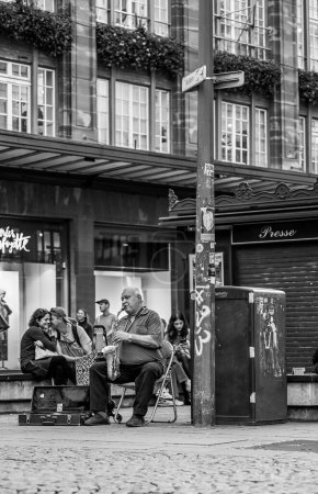 Téléchargez les photos : Une échelle de gris verticale d'un musicien masculin jouant de la musique de jazz dans une rue, les gens en arrière-plan - en image libre de droit