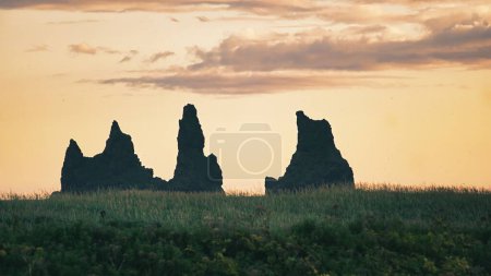 Photo for The silhouettes of rocky formations in a green field before the sunset skyline - Royalty Free Image