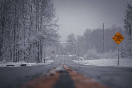 Téléchargez les photos : Un gros plan d'une route et une pancarte jaune lisant les glaces du pont avant la route par une froide journée d'hiver - en image libre de droit