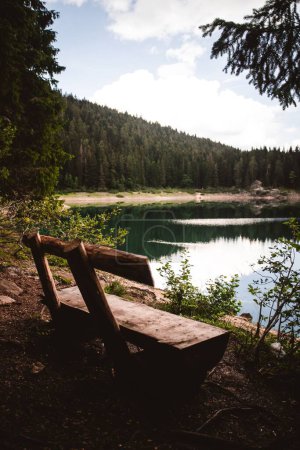 Photo for A vertical shot of the Black lake with a wooden chair at the edge surrounded by Durmitor mountains in Zabljak, Montenegro - Royalty Free Image