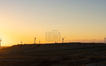 Foto de Una silueta de molinos de viento en un campo de hierba bajo un cielo degradado al atardecer - Imagen libre de derechos