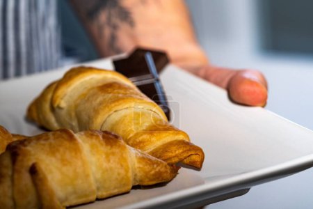 Foto de Una vista de cerca de croissants con barras de chocolate negro en un plato en la mano del chef - Imagen libre de derechos