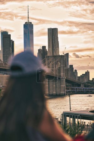 Foto de Un disparo vertical del puente de Brooklyn contra un cielo nublado al atardecer con una mujer desenfocada en primer plano - Imagen libre de derechos