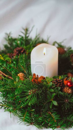 Photo for A vertical shot of a candle with a pine tree wreath on white fabric - Royalty Free Image