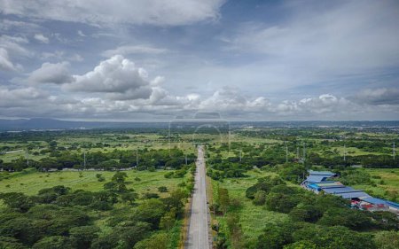 Photo for An aerial view of long asphalt road stretching through lush green rural areas with scattered buildings - Royalty Free Image