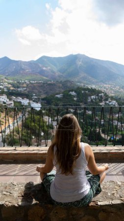 Téléchargez les photos : Un plan vertical d'une femme caucasienne méditant avec de grandes montagnes en arrière-plan par une journée ensoleillée - en image libre de droit