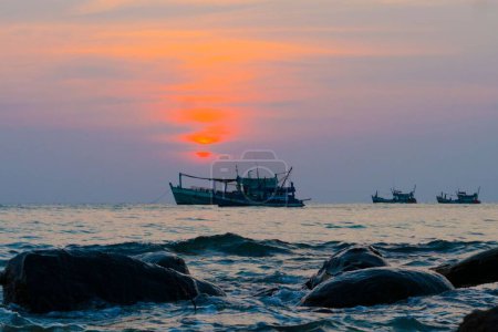Téléchargez les photos : Quelques bateaux de pêche nageant en mer au coucher du soleil fond de ciel violet - en image libre de droit