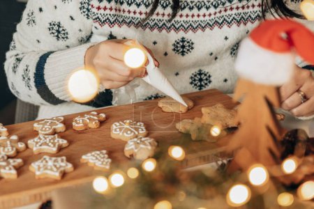 Téléchargez les photos : Femme tenant sac de tuyauterie, décoration maison biscuits de Noël cuits au four avec glaçage royal blanc - en image libre de droit