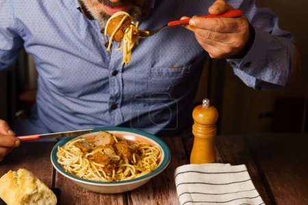 Foto de Hombre con barba y camisa azul comiendo albóndigas con espaguetis en un restaurante - Imagen libre de derechos