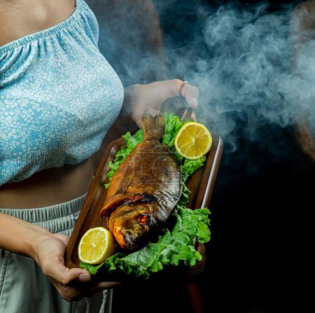 Photo for A closeup shot of a female serving a board with a gourmet steaming smoked fish with lemons - Royalty Free Image