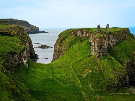Foto de El castillo Dunseverick con hierba verde sobre acantilados rocosos fondo sombrío paisaje marino - Imagen libre de derechos