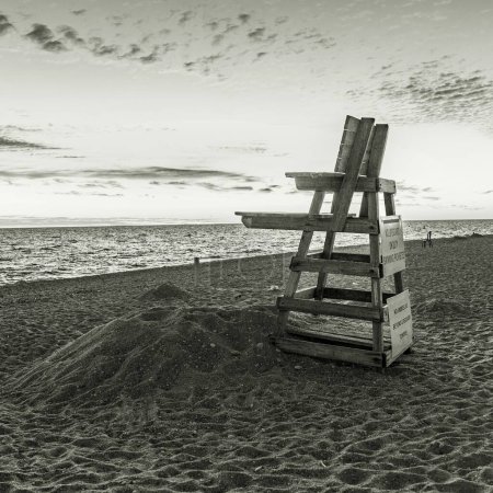 Téléchargez les photos : Une échelle de gris d'une grande chaise de sauveteur en bois avec des signes sur le dos à une plage surplombant l'océan Atlantique - en image libre de droit