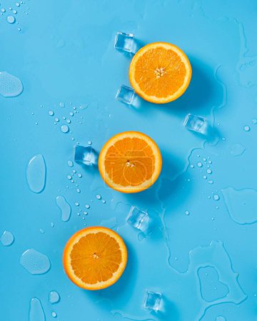 Photo for A vertical top view of orange slices with a ice cubes on a blue background - summer concept - Royalty Free Image