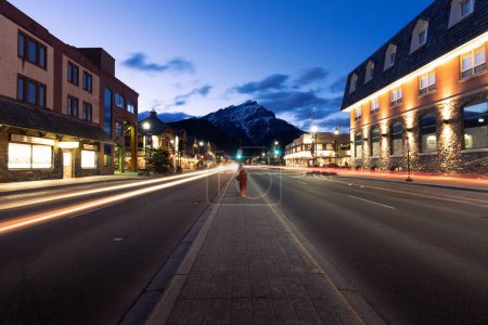 Téléchargez les photos : Vue panoramique d'une route vide entourée de bâtiments éclairés pendant la nuit à Banff, en Alberta - en image libre de droit
