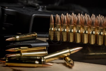 Foto de Varias balas de munición de 223 (5.56x45mm) en un cargador cargado junto a un AR-15 - Imagen libre de derechos