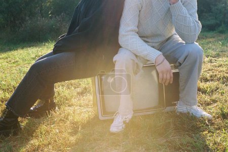 Téléchargez les photos : Un gros plan des pieds d'un couple assis sur une télévision vintage sur l'herbe - en image libre de droit