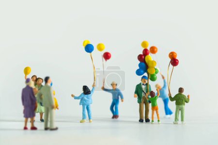 Foto de Un primer plano de figuras en miniatura de un hombre y niños con globos de aire aislados sobre un fondo blanco - Imagen libre de derechos
