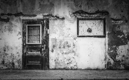Téléchargez les photos : Échelle de gris d'une porte en bois altérée d'un mur fissuré dans une zone urbaine - le concept de pauvreté - en image libre de droit