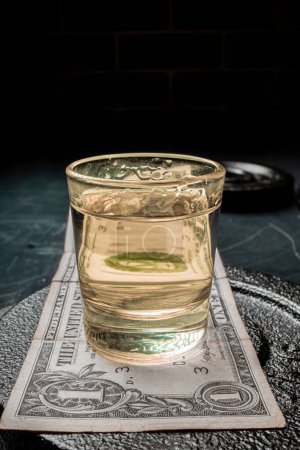 Téléchargez les photos : Plan vertical d'un verre de tequila sur un billet d'un dollar sur une plaque métallique - en image libre de droit