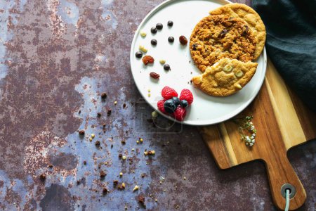 Téléchargez les photos : Une vue de dessus des biscuits avec des baies dans une assiette blanche sur une planche en bois - en image libre de droit