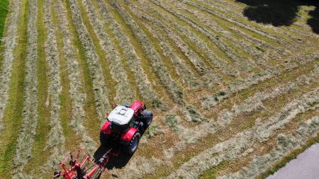 Foto de Vista aérea de un tractor montado con rastrillos giratorios que se mueven a través de un campo de hierba de heno - Imagen libre de derechos