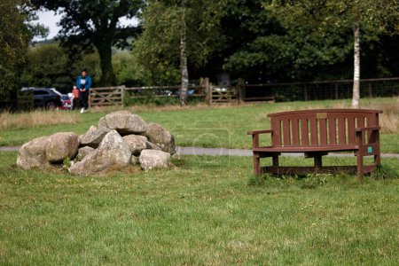 Téléchargez les photos : Un banc en bois dans le parc verdoyant avec une pile de rochers à côté - en image libre de droit