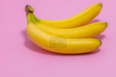 Foto de Un primer plano de una mano de plátano amarillo brillante y su sombra sobre un fondo rosa - Imagen libre de derechos