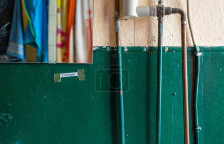 Téléchargez les photos : Un gros plan d'un vieux mur vert avec des tuyaux et un petit miroir et une petite note - en image libre de droit