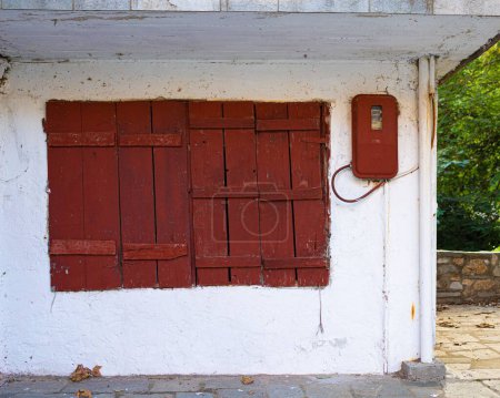 Foto de Una ventana roja de madera y una caja de contadores eléctricos en una vieja pared blanca. - Imagen libre de derechos