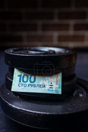 Photo for A vertical shot of 100 Russian rubles (Olympic edition) note between metal plates on a table - Royalty Free Image