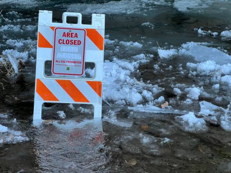 Photo for An "area closed" board on a flowing water, melting snow around - Royalty Free Image