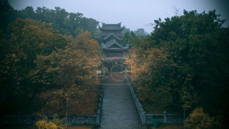 Photo for A Chinese temple with orange paper lamps by the entrance surrounded by dark trees on a gloomy fall day - Royalty Free Image